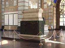 A white marble sarcophagus elevated on a black pedestal, inside  a chapel