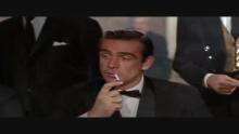 Video clip from the film, set in a casino. A woman at the table, wearing a red dress, asks "Mister ...?" and a man in a suit answers "Bond, James Bond" as he lights his cigarette.