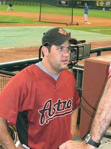 A man in a red baseball jersey with "ASTROS" on the chest and black cap stands in a baseball dugout looking up.