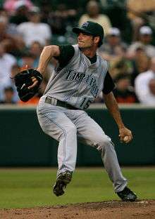 A man in a green baseball cap and grey baseball uniform with "TAMPA BAY 15" on the chest prepares to pitch a baseball with his left hand.