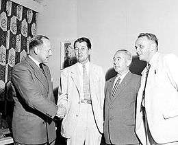 Four men in civilian clothes, two of whom are shaking hands