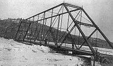 A black and white photograph of a truss bridge with large pack ice and ice floes in the river below