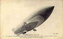 An airship with a pointed prow is seen from below; the gondola is visible, as are two ailerons, one port, one starboard