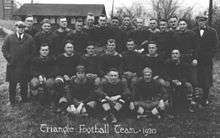 A group of men standing in rows of three in their football uniforms. One executive is all the way to the left, and the other executive is on the right. The words "Triangle Football Team, 1920" is written on the photograph.
