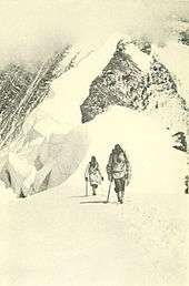 Photo of two men trudging out of a snowy, mountainous background