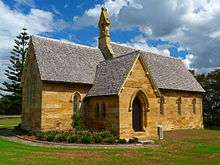 Photo of a little sandstone church with an unaisled nave, a projecting chancel, a porch, and topped with a small gabled belfry.