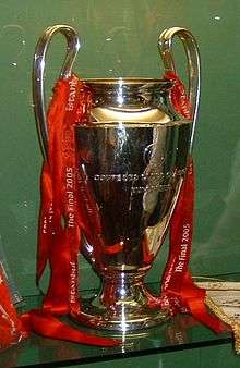 A silver trophy with red ribbons on it, set against a green background