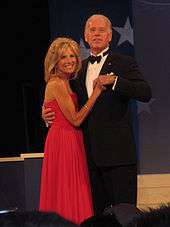 A Caucasian man in a tuxedo dances with a blonde woman in a red dress.