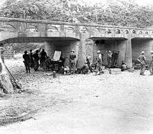 A group of soldiers around a makeshift office under a bridge