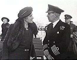 Woman in dark coat and hat talking with man in dark military uniform