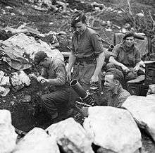 Four men in berets and shirtsleeves in a mortar pit