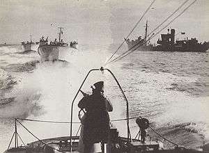three Motor Gun Boats at sea in line astern passing a merchant ship