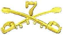 A computer generated reproduction of the insignia of the Union Army 7th Regiment cavalry branch. The insignia is displayed in gold and consists of two sheafed swords crossing over each other at a 45 degree angle pointing upwards with a Roman numeral 7