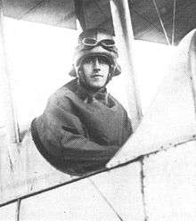Half-portrait of man in flying helmet and goggles seated in the open cockpit of a biplane