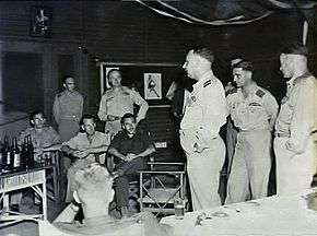 Ten men in military uniforms and fatigues talking in a room
