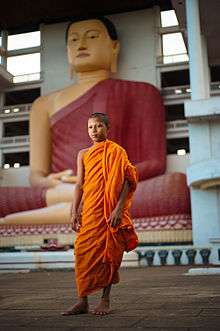 A young monk in saffron robes standing in Sri Lanka temple