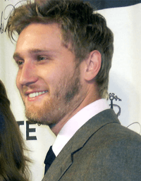 A 27-year old, dark-haired, bearded man, smiling to the left of the camera.