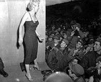 Monroe standing on a podium wearing a tight dress and high-heeled sandals, greeting a crowd of US Marines