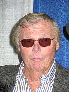 A man with light colored hair and sunglasses, looks straight forward, with a shocked look on his face.