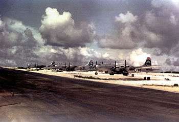 Color photo of three silver four engined World War II-era aircraft neatly lined up alongside a runway