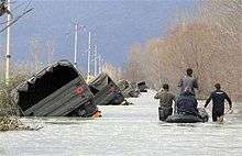 Albanian army rescuers and villagers pass by a convoy of trucks pushed to the side of the road by flood water on the outskirts of Bahcallek, near the city of Shkodra, Sunday, January 10, 2010.