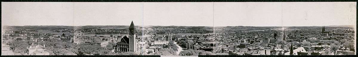 A panorama from 1909, in sepia, shows a view of the city perpendicular to the river; there are numerous church steeples and the city hall tower can be seen left of center.