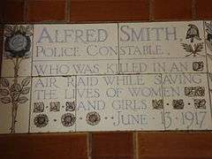 A tablet formed of five tiles of varying sizes, bordered by yellow and blue flowers in an art nouveau style
