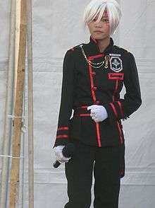 A young person doing a cosplay wearing a black and red uniform and a white wig.
