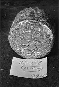A rough-surfaced cylinder of metal with a paper in front of it, like a label