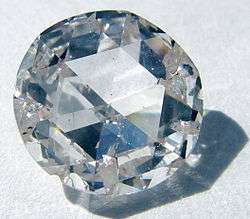 A round, clear gemstone with many facets, the main face being hexagonal, surrounded by many smaller facets.