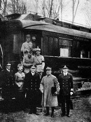 black and white photograph of five men in military uniforms standing side-to-side in front of a railcar. Four men are disembarking behind them.