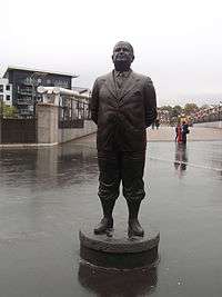 A bronze-statued Herbert Chapman, standing with hands behind his back. The statue was erected to commemorate his time at Arsenal.
