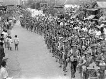A large body of soldiers in column of route march through a town