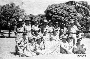 A group of soldiers in slouch hats pose with a Japanese flag.