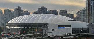 A distant shot shows a large domed arena set in front of a city skyline.