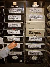 Two vertical columns of binds holding records in paper sleeves for sale. Lettering identifying each bin is by hand.