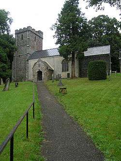 Stone building with square tower, partially obscured by trees.