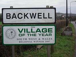 Road signs with Backwell in black writing on white background and below it another sign saying village of the year South West and Wales regional winner 1997.