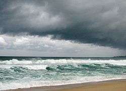 A beach is battered by choppy seas from an offshore storm and overcast, dark skies hang overhead.