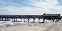 A long building built on a narrow pier extending out from the beach to the ocean.