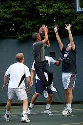 Obama about to take a shot while three other players look at him. One of those players is holding is arms up in an attempt to block Obama.