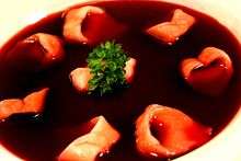 A bowl of clear dark-red broth with small ear-shaped mushroom-filled dumplings