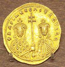 A photograph of a gold coin depicting two crowned figures, both grasping a double-barred patriarchal cross between them