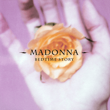 An orange flower is held in the palm of a white hand in front of a purple background with the artist and the song name written on top of it.