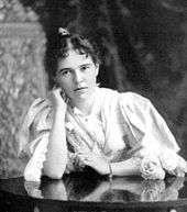 Photo of Blanche Blick Burnham taken in 1896 in Bulawayo, Rhodesia. She is seated at a table and her head is leaning on her right arm.  She is wearing a flowing dress.