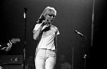 A black and white photograph of Debbie Harry on stage with a microphone