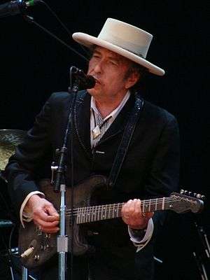 Bob Dylan plays a guitar and sings into a microphone
