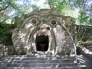 A moss-covered sculpture of an ogre's head in a garden.