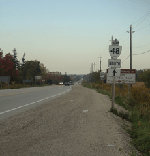 A two-lane undivided road in a rural area with a reassurance marker for Ontario Highway 48 north pointing straight