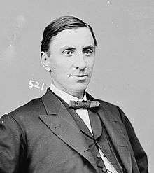 A man with dark hair wearing a dark jacket, vest, and bowtie and a white shirt